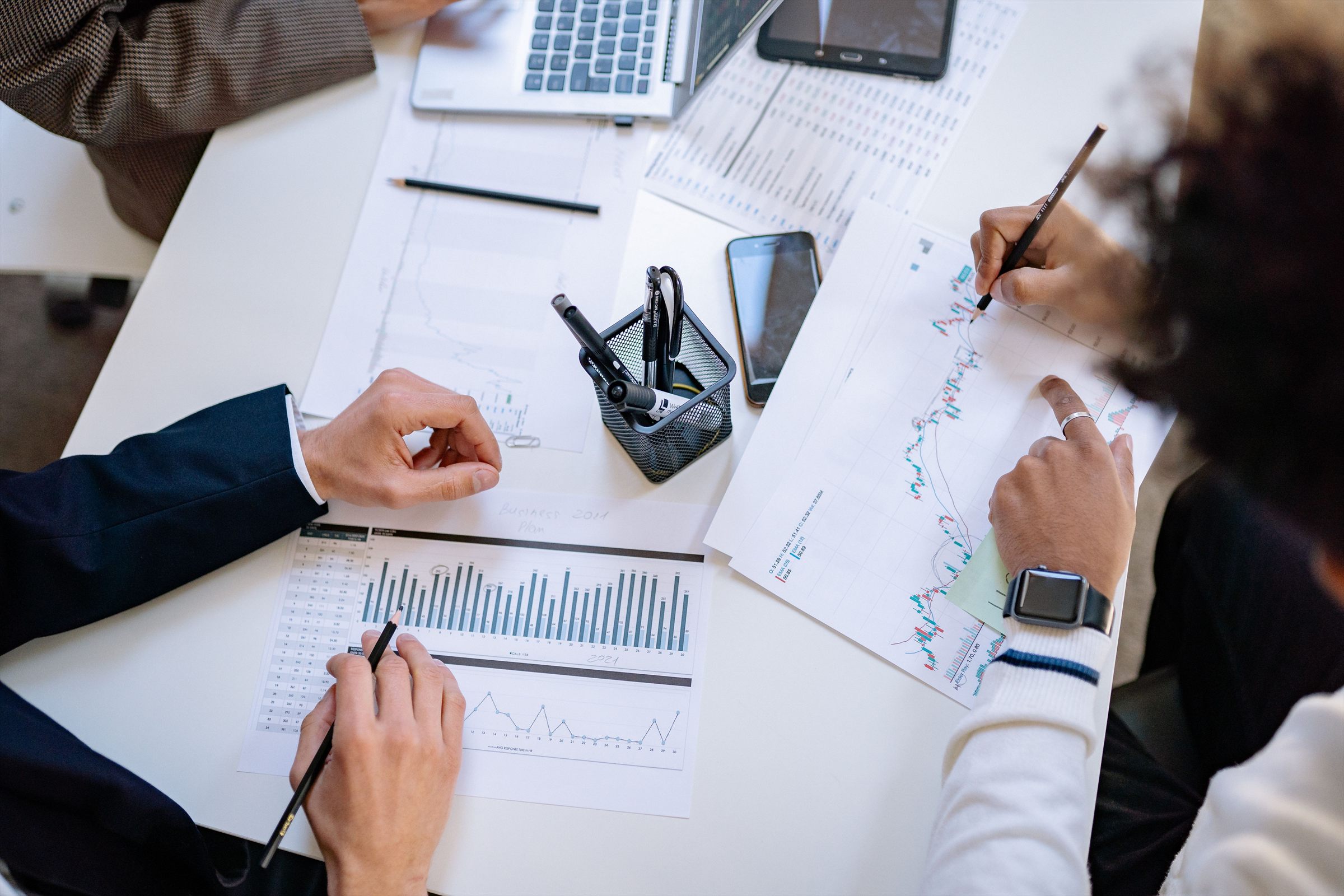 Hands marking up printed charts on a desk, seen from above